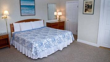 A bedroom with a large bed, a nightstand, a dresser, a mirror, and a door.