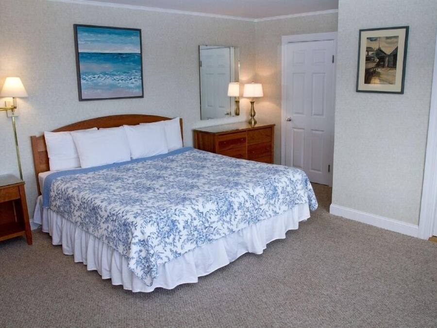 A bedroom with a large bed, a nightstand, a dresser, a mirror, and a door.
