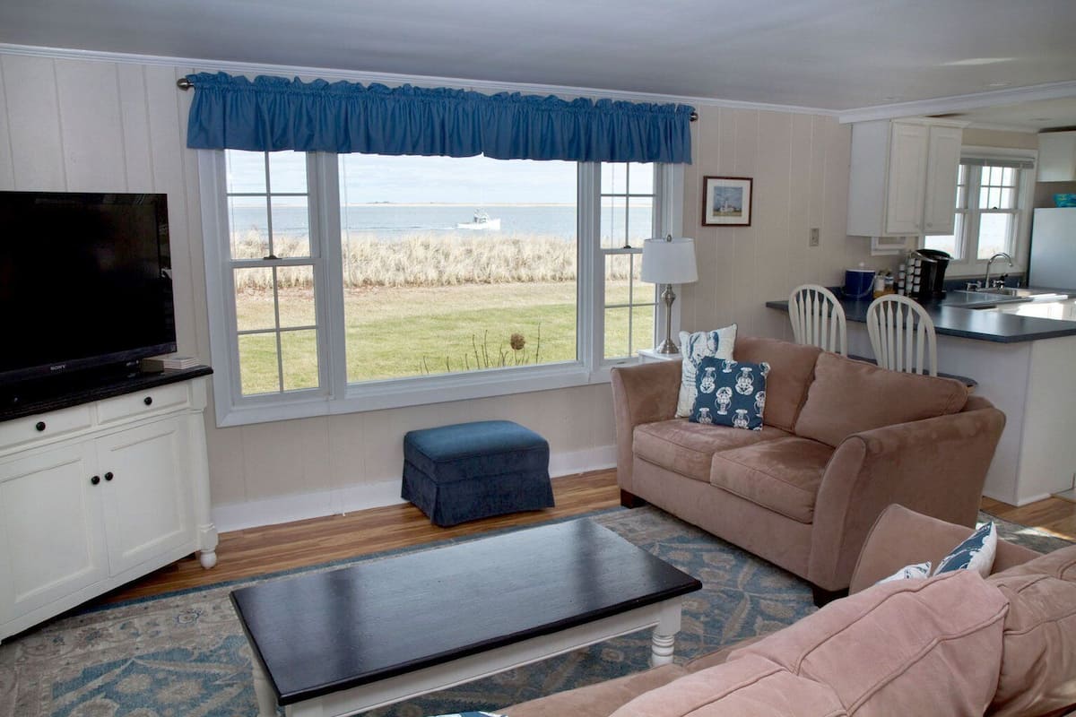 A living room with a television, a sofa, a coffee table, and a view of the sea through large windows.
