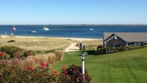 A coastal view with a beach, boats, and a house with a lawn and lamp post. - The Hawthorne (Chatham)