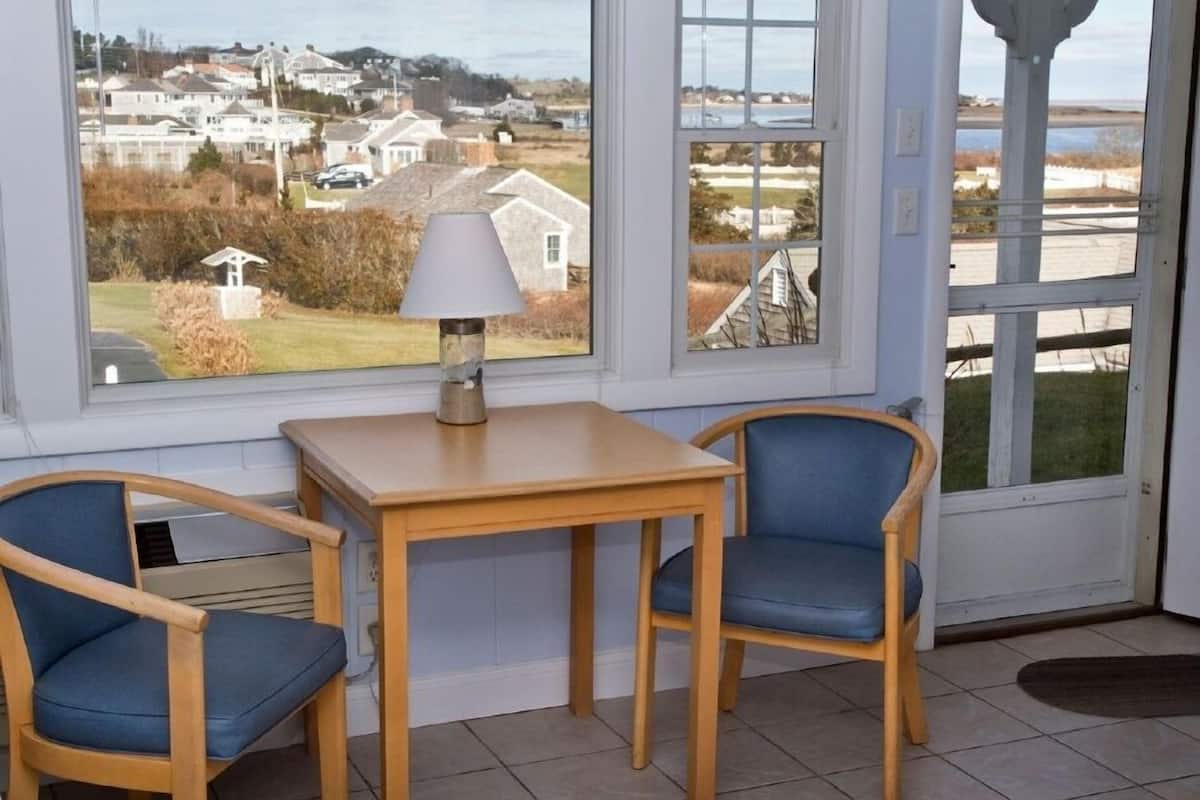 A room with a window view of a residential area, a table, two chairs, and a lamp.