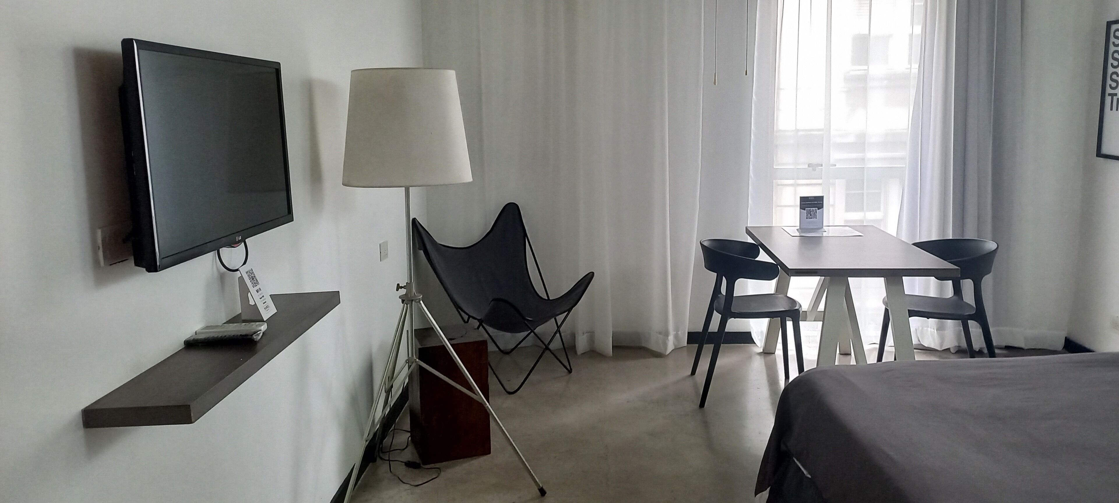 A hotel room with a flat-screen TV, a desk with two chairs, a lamp, and a bed.