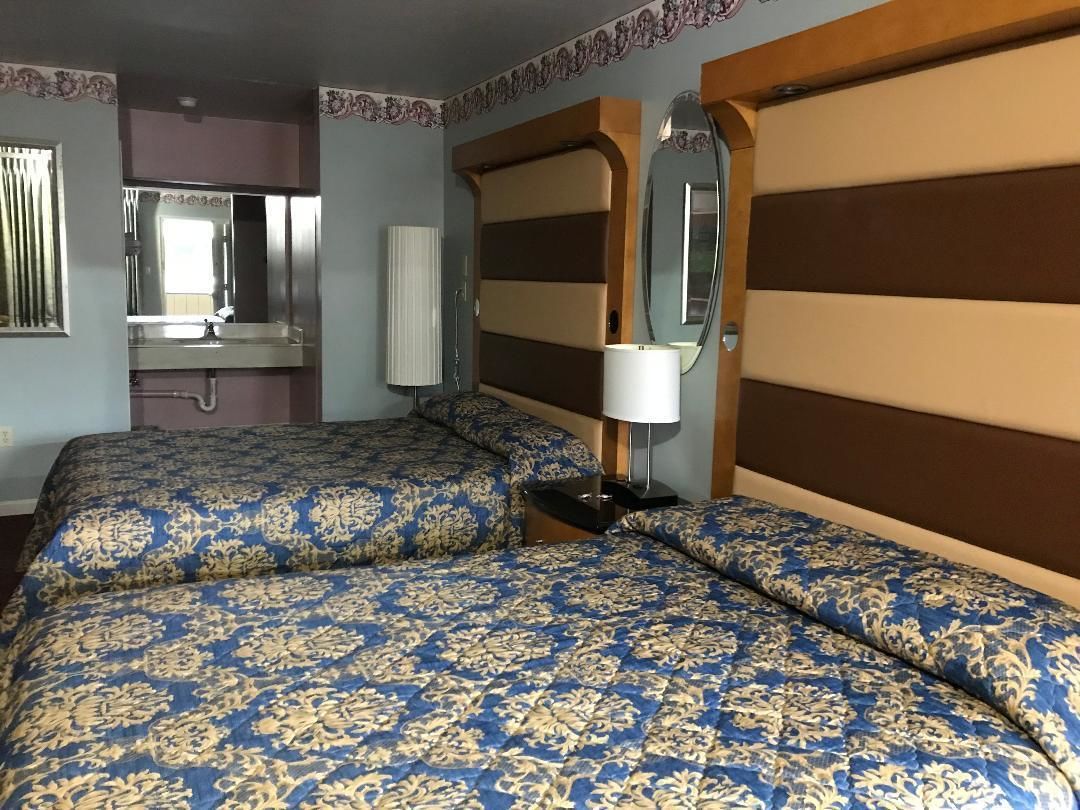 A hotel room with a large bed, a bedside table with a lamp, a mirror, and a bathroom visible through an open door.