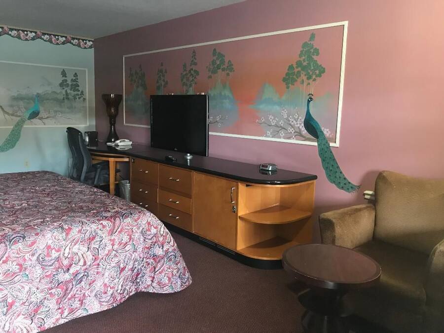 Habitación de hotel con una cama, un escritorio con computadora, televisor, una silla y una mesita.