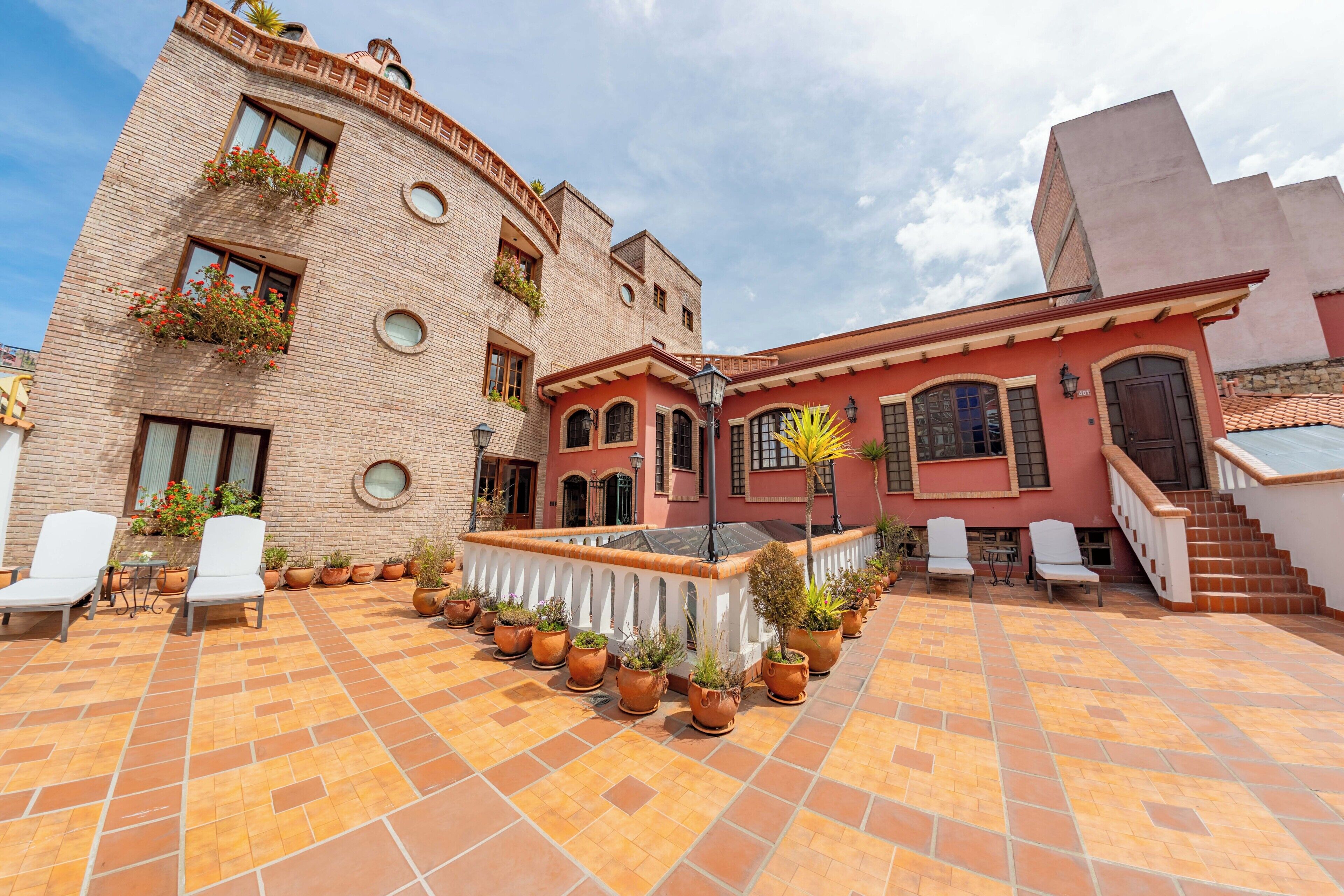 A courtyard with tiled flooring, potted plants, and white chairs.