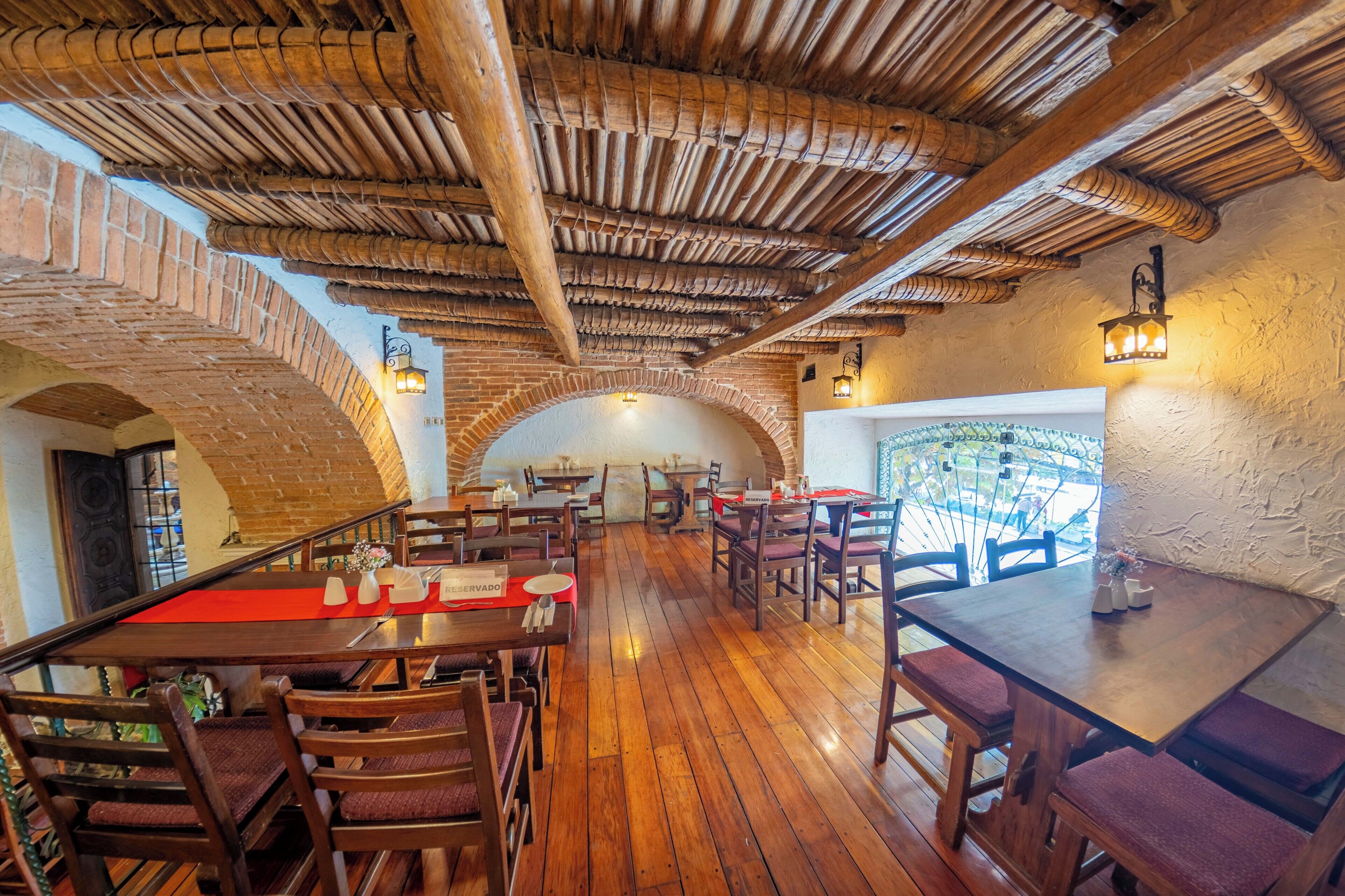 A restaurant with wooden floors, brick arches, and a thatched roof. Tables are set with red placemats and candles.