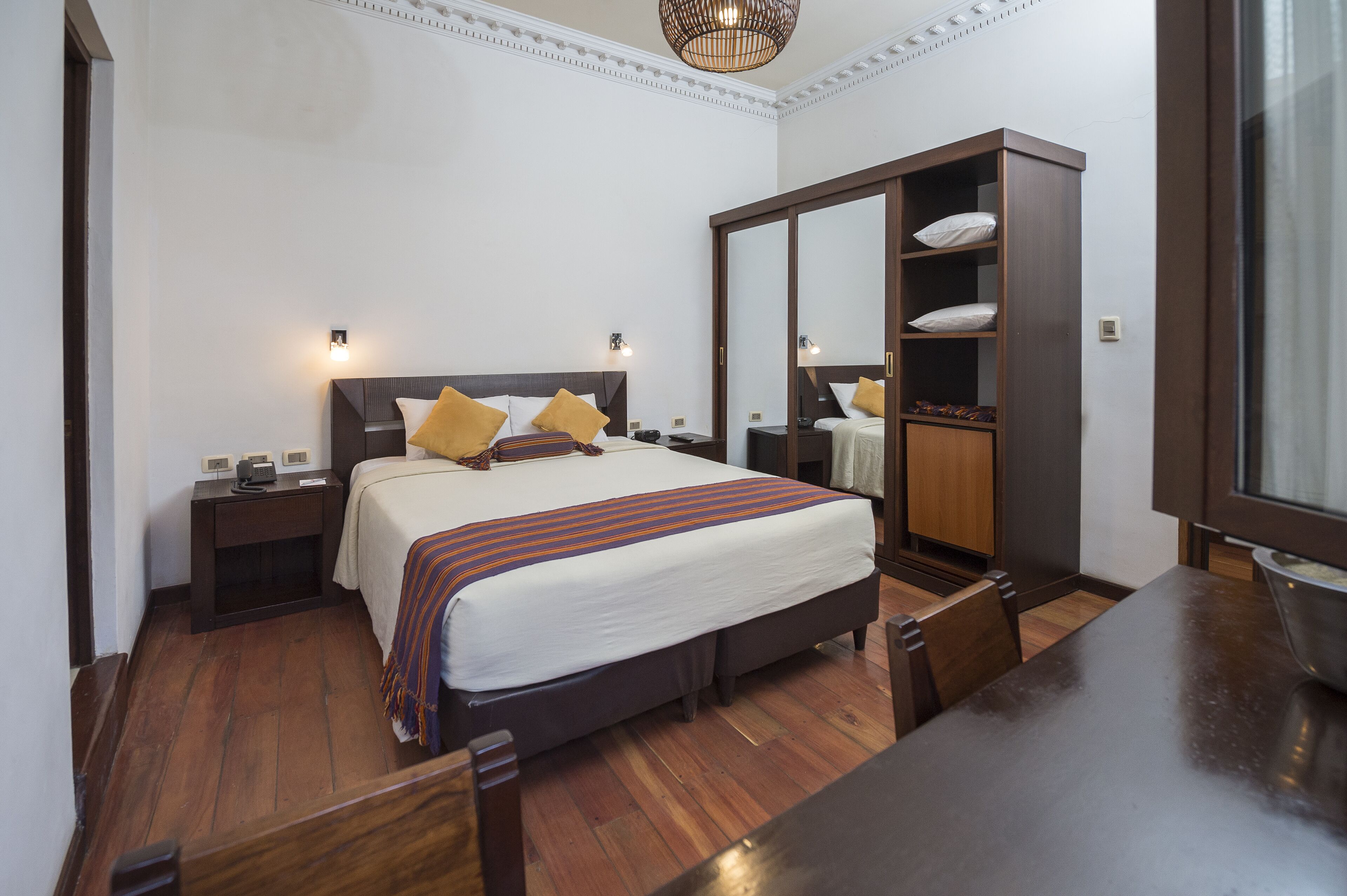Habitación de hotel con cama, mesitas de noche, armario, mesa de comedor y candelabro.