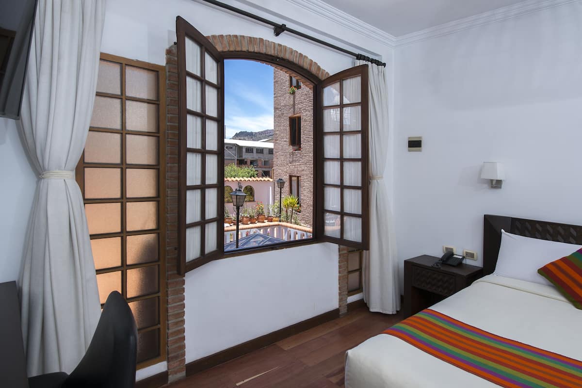 A hotel room with a large window, a bed, a nightstand, and a chair.