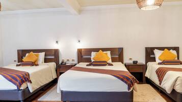 A hotel room with three beds, each with a wooden headboard, white bedding, and a striped throw blanket.