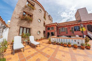 Un patio con un edificio de ladrillo, mobiliario exterior y plantas en macetas.