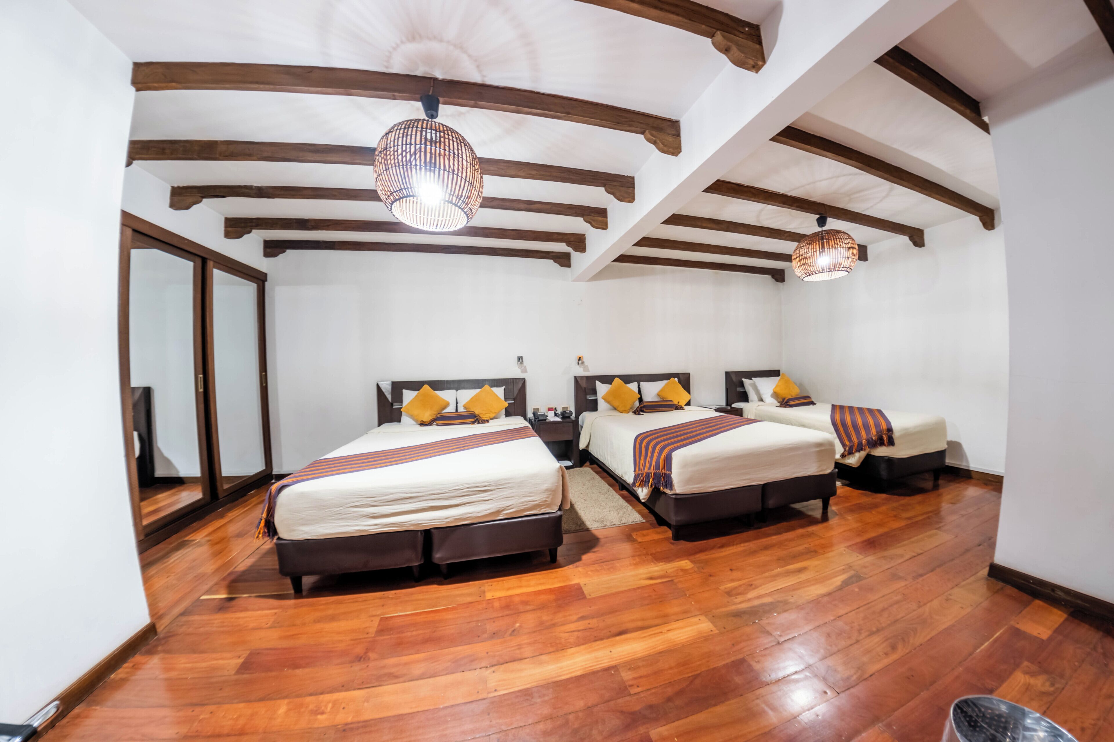 A hotel room with two beds, wooden flooring, and a sloped ceiling with exposed beams.