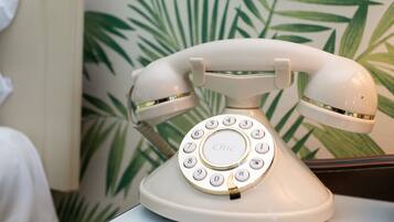 Un teléfono blanco de disco giratorio con la palabra 'Chic' en el dial, colocado sobre una mesa con un papel tapiz de hojas de palma.
