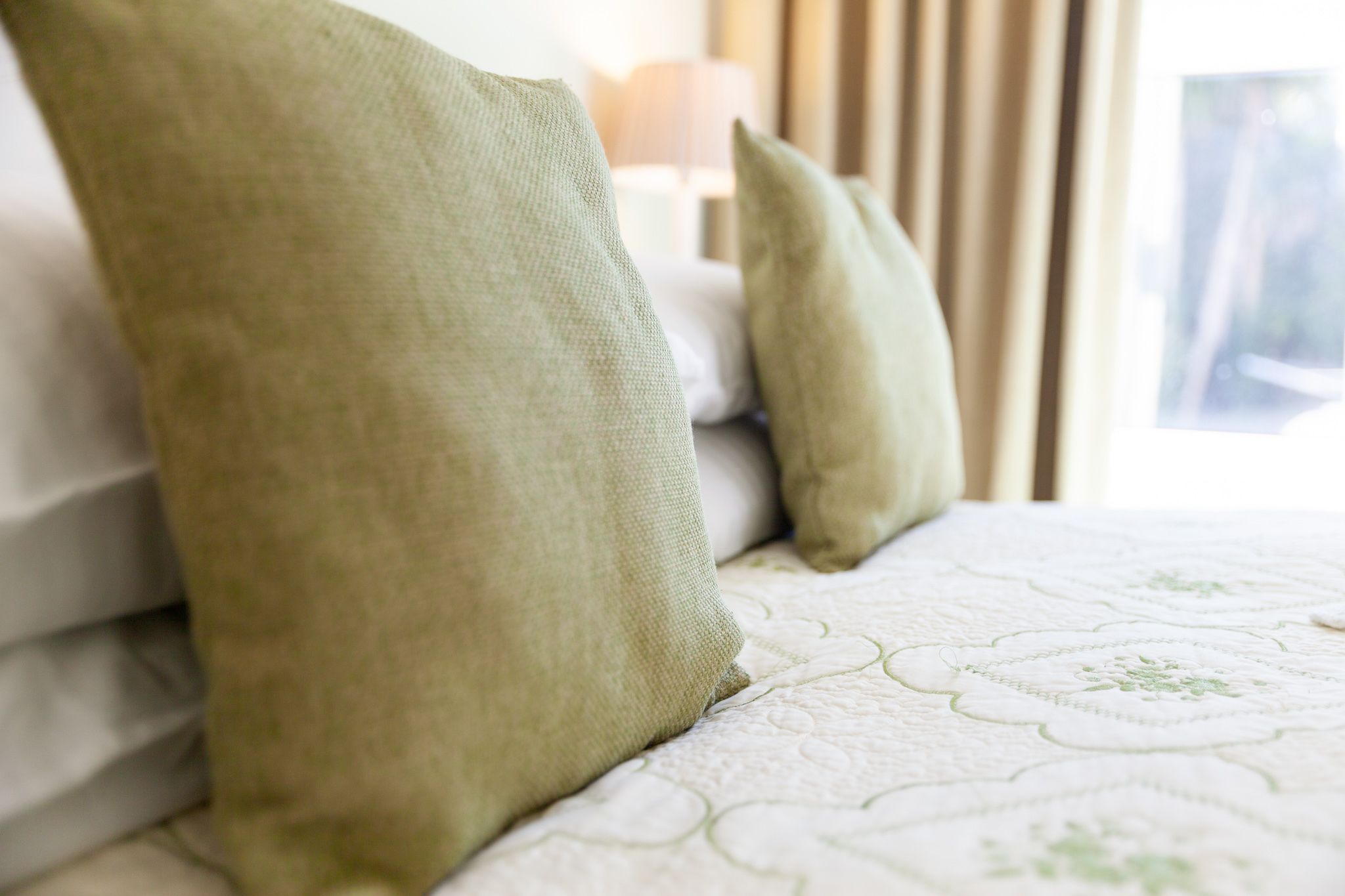 Una cama con colcha blanca y almohadas verdes.
