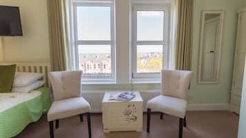 Ein Schlafzimmer mit zwei weißen Stühlen, einem kleinen Tisch mit einem Buch und einem Bett mit einer grünen Tagesdecke.