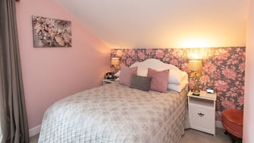 Een slaapkamer met een bed, nachtkastjes, een lamp, een stoel en bloemenbehang.