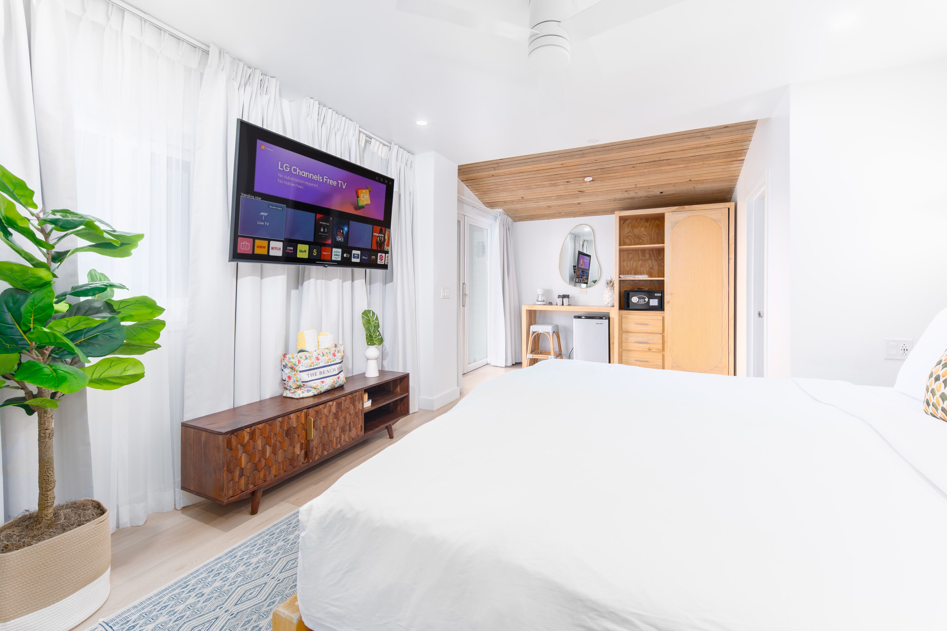 A modern hotel room with a large bed, a flat-screen TV mounted on the wall, a wooden cabinet, and a potted plant.