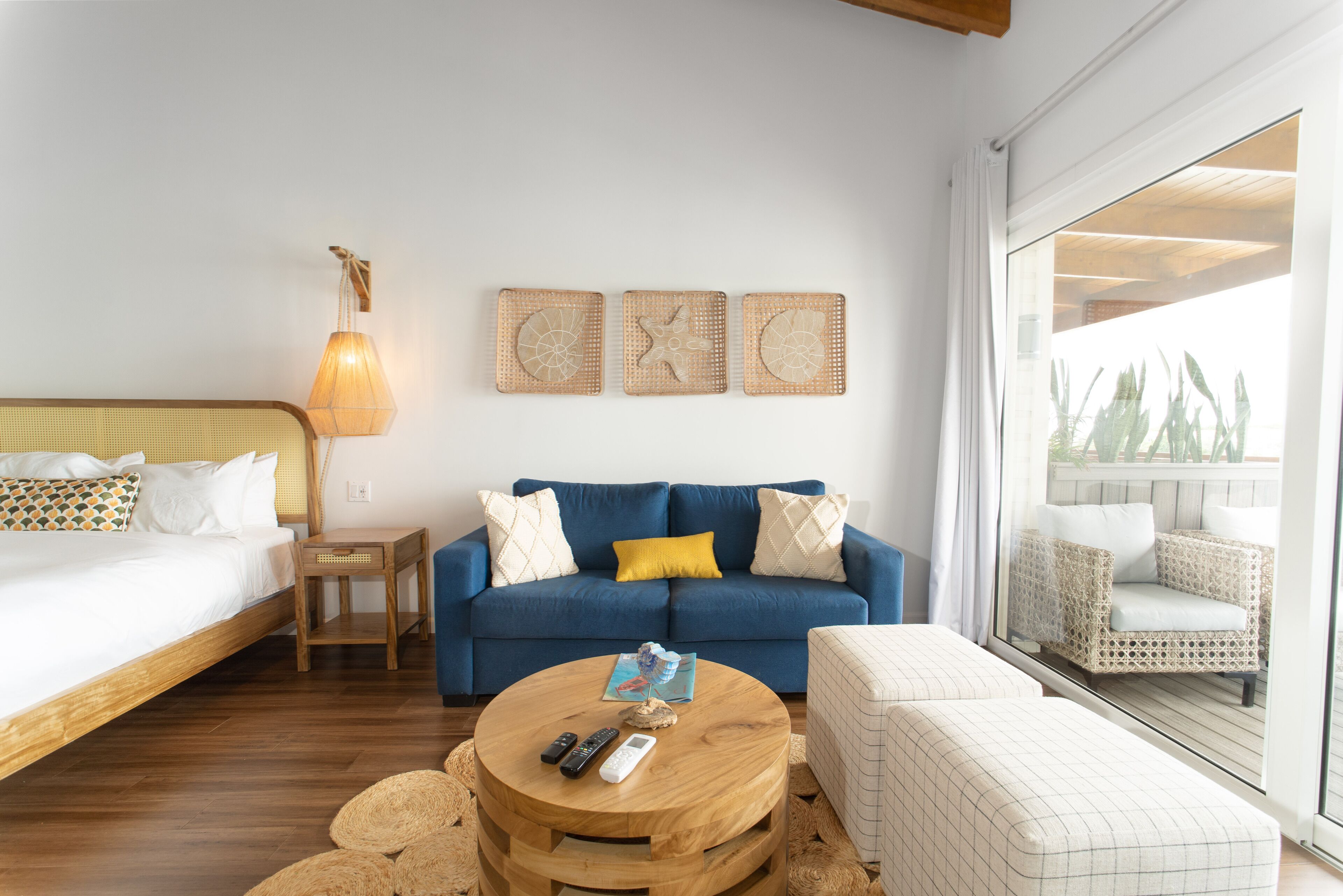 Una habitación de hotel con cama, sofá azul, mesa redonda de madera y balcón amueblado con ratán.