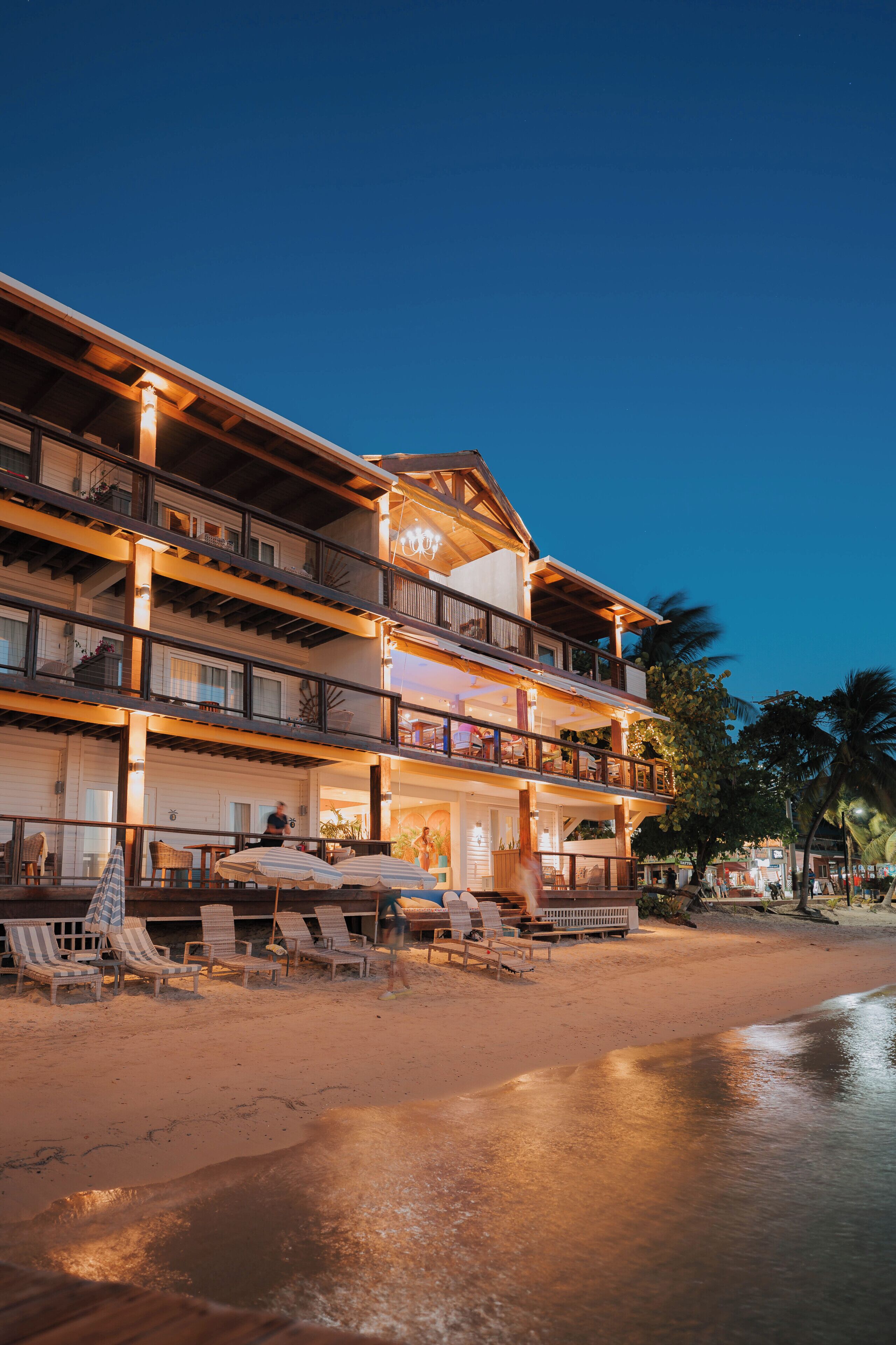 A multi-story hotel with balconies, outdoor seating, and a beach view.