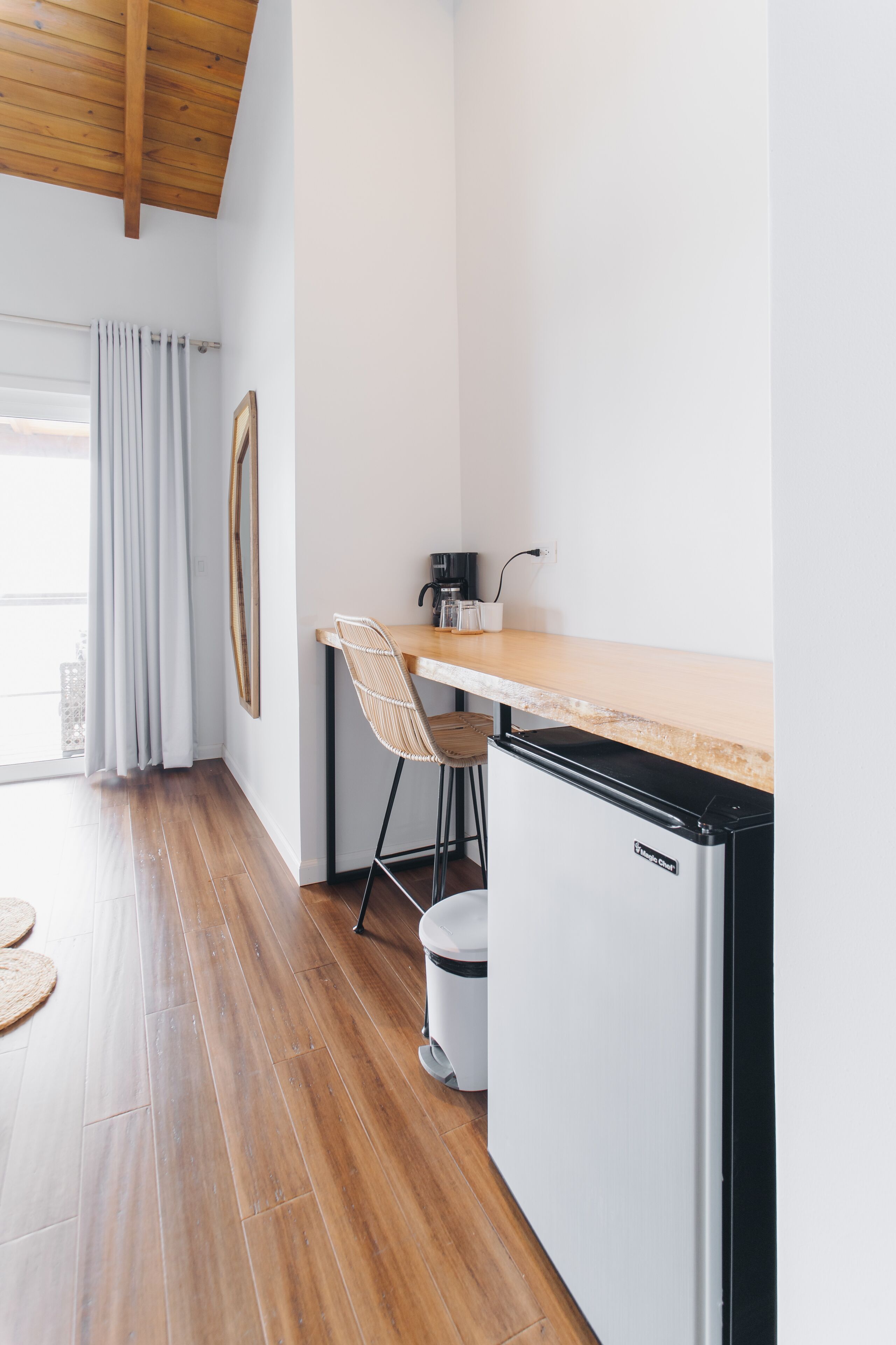Cocina compacta con encimera de madera, refrigerador blanco, taburete de bar y una ventana con cortinas.