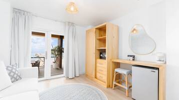 Una habitación moderna con puerta de vidrio corredera que da a un balcón, una kitchenette pequeña y un espejo grande en la pared.