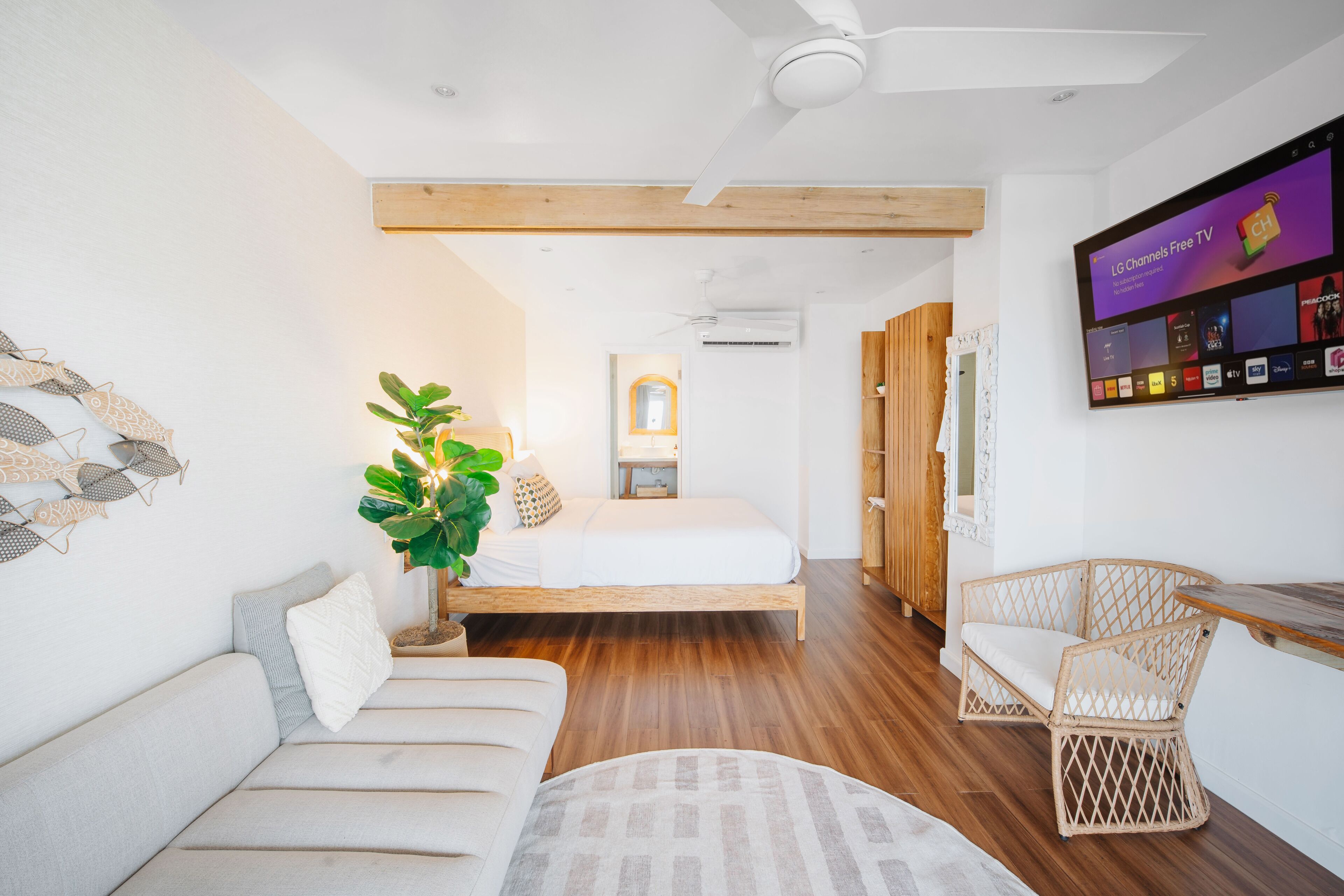 A modern, well-lit room with a bed, a sofa, a wicker chair, and a flat-screen TV displaying LG Channels Free TV.