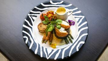 Un plato de comida con varias verduras y una taza pequeña de salsa sobre una mesa oscura.