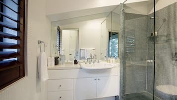 Un baño moderno con un espejo grande, muebles blancos, cabina de ducha de vidrio y vistas al exterior.