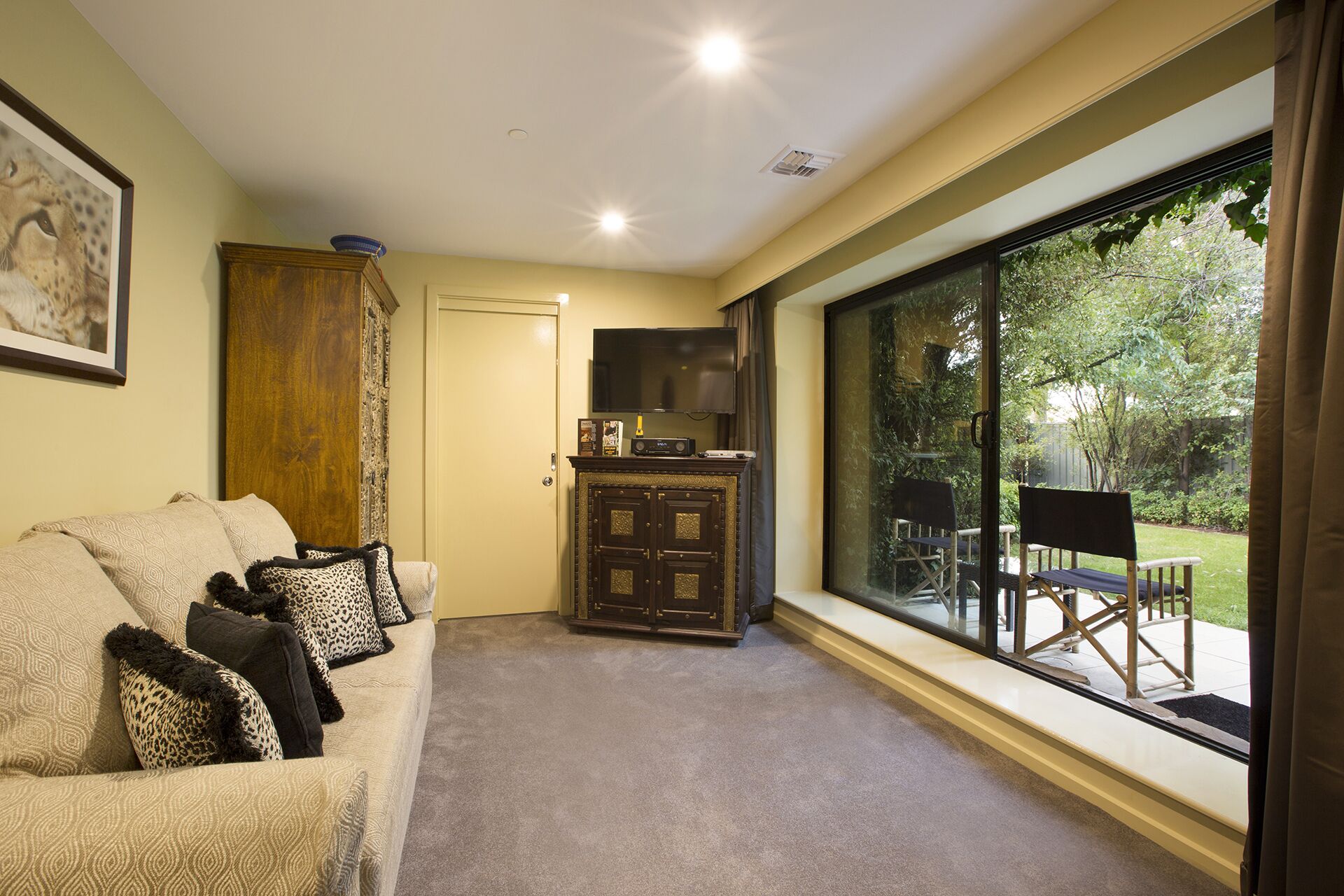 A cozy living room with a sofa, a cabinet, and a television. There is a large window offering a view of the outdoors.