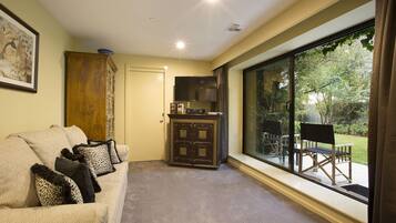 A cozy living room with a sofa, a cabinet, and a television. There is a large window offering a view of the outdoors.