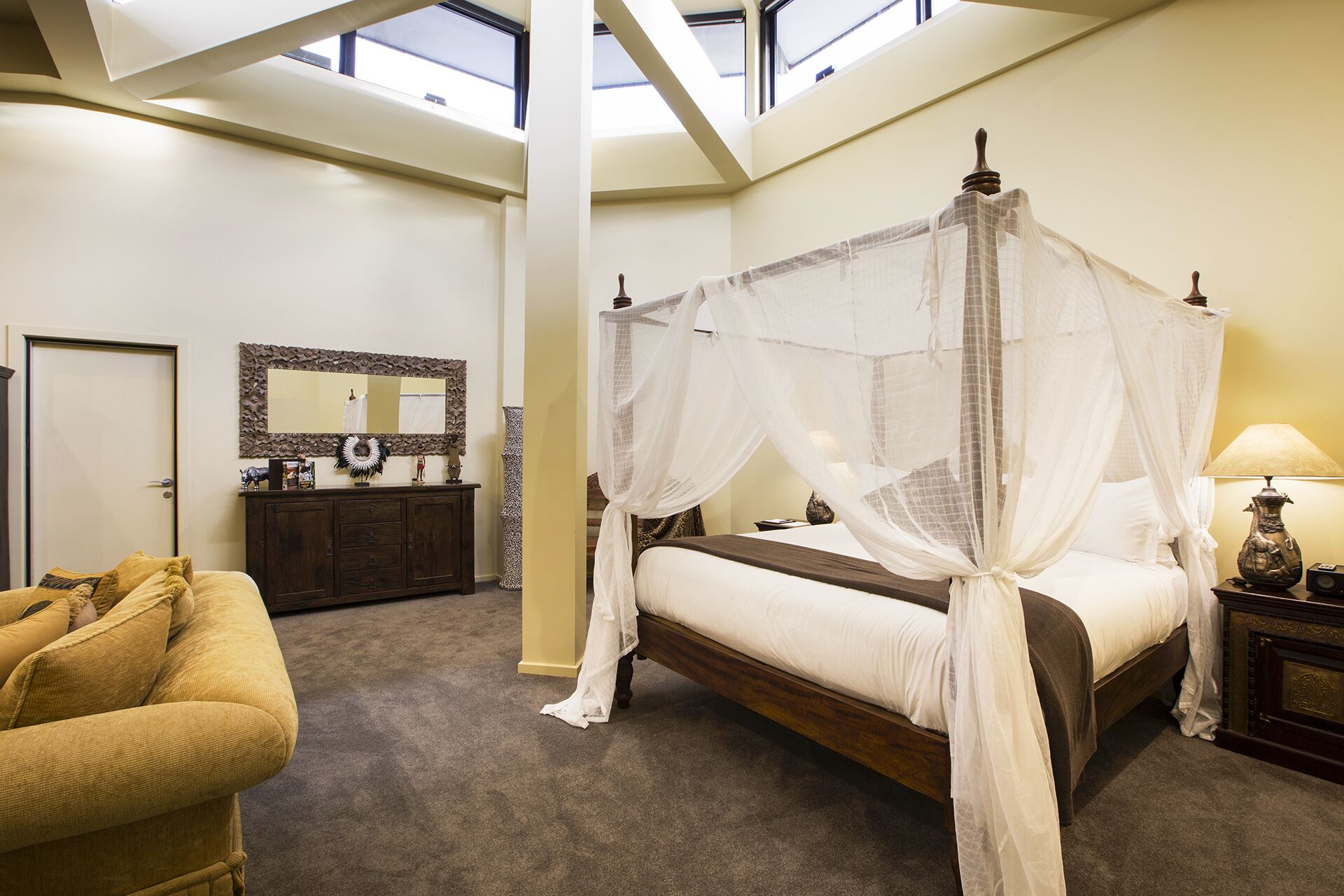 A bedroom with a four-poster bed, a wooden dresser, a mirror, and a sofa.
