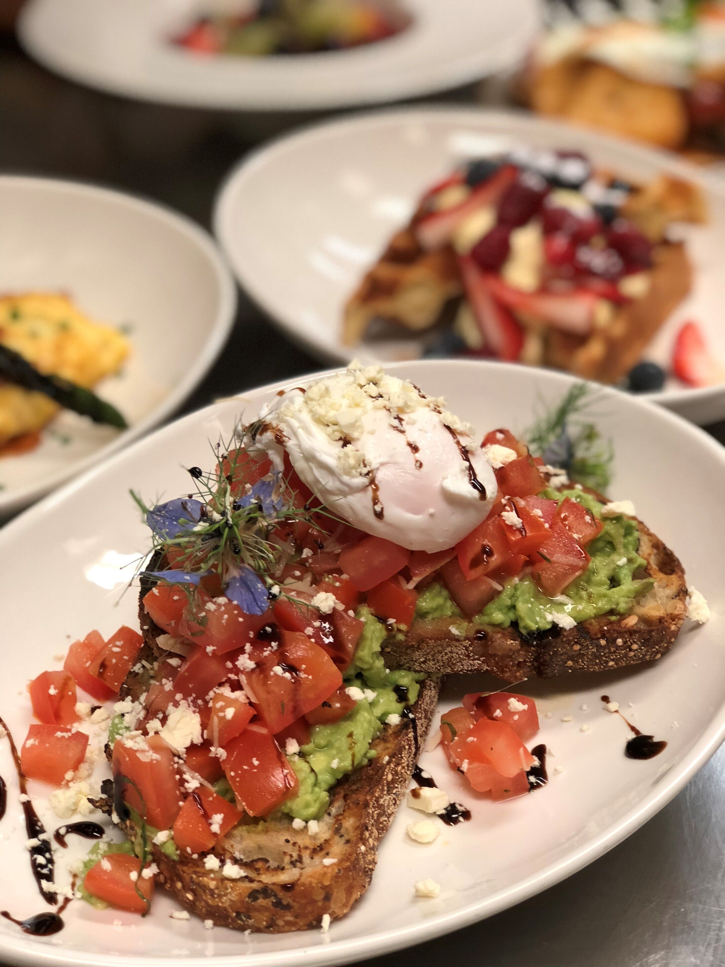 A plate of bruschetta topped with tomatoes, guacamole, cheese, and a poached egg.