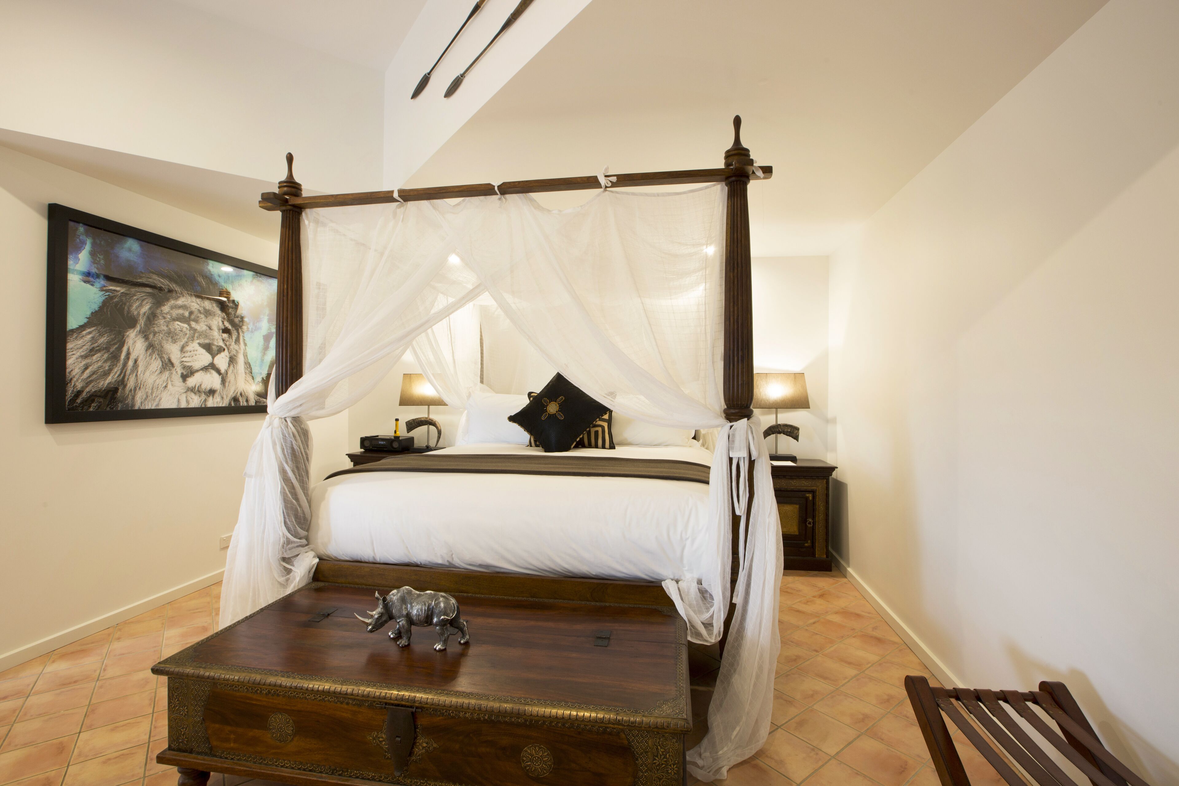 A four-poster bed with a canopy, a framed lion painting on the wall, a bedside table with a lamp, and a nightstand with a lamp.