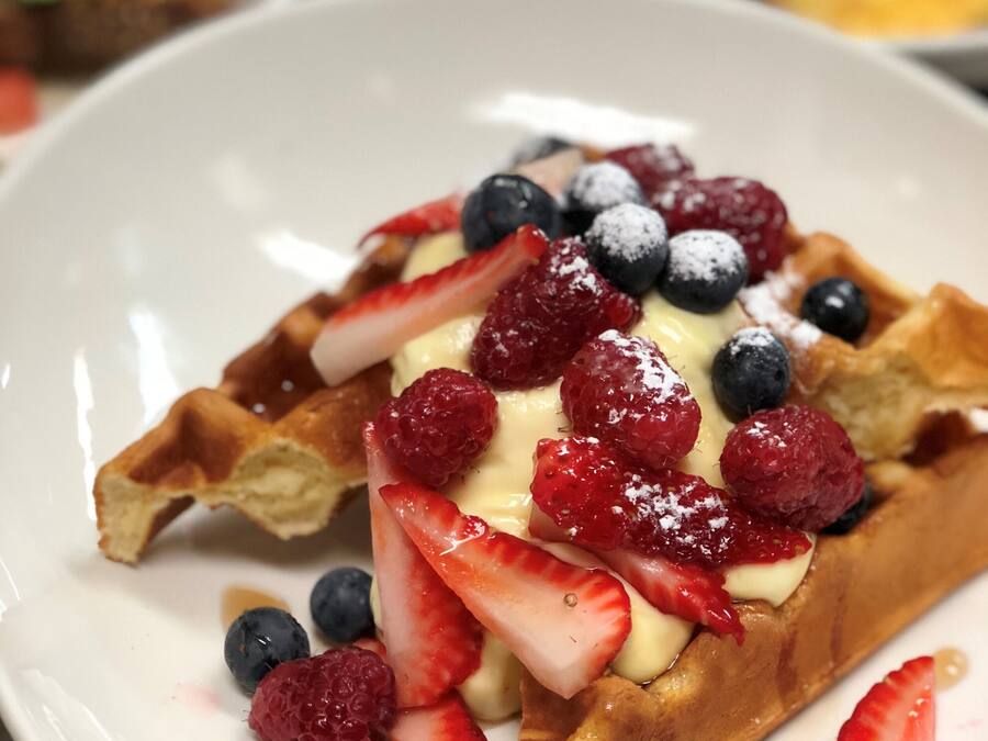 Gofre cubierto con fresas, arándanos y frambuesas, servido en un plato blanco.