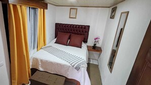A bedroom with a bed, a nightstand, a mirror, and a window with curtains. - Monteverde Coati & Sloth Studios Apartments (Monteverde)