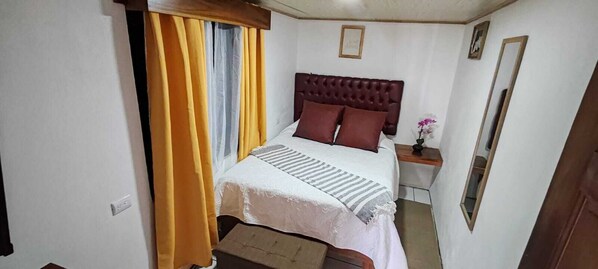 A bedroom with a bed, a nightstand, a mirror, and a window with curtains. - Monteverde Coati & Sloth Studios Apartments (Monteverde)
