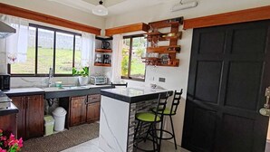 A compact kitchen with a central island, a microwave, a toaster, and a sink. There are wooden shelves above the sink and a black door to the right. - Monteverde Coati & Sloth Studios Apartments (Monteverde)