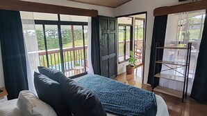 A bedroom with a bed, a window with curtains, a balcony with a chair, and a potted plant. - Monteverde Coati & Sloth Studios Apartments (Monteverde)