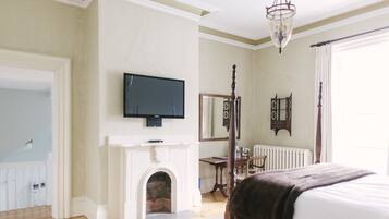 Un dormitorio con cama, televisión, chimenea, espejo y ventana.