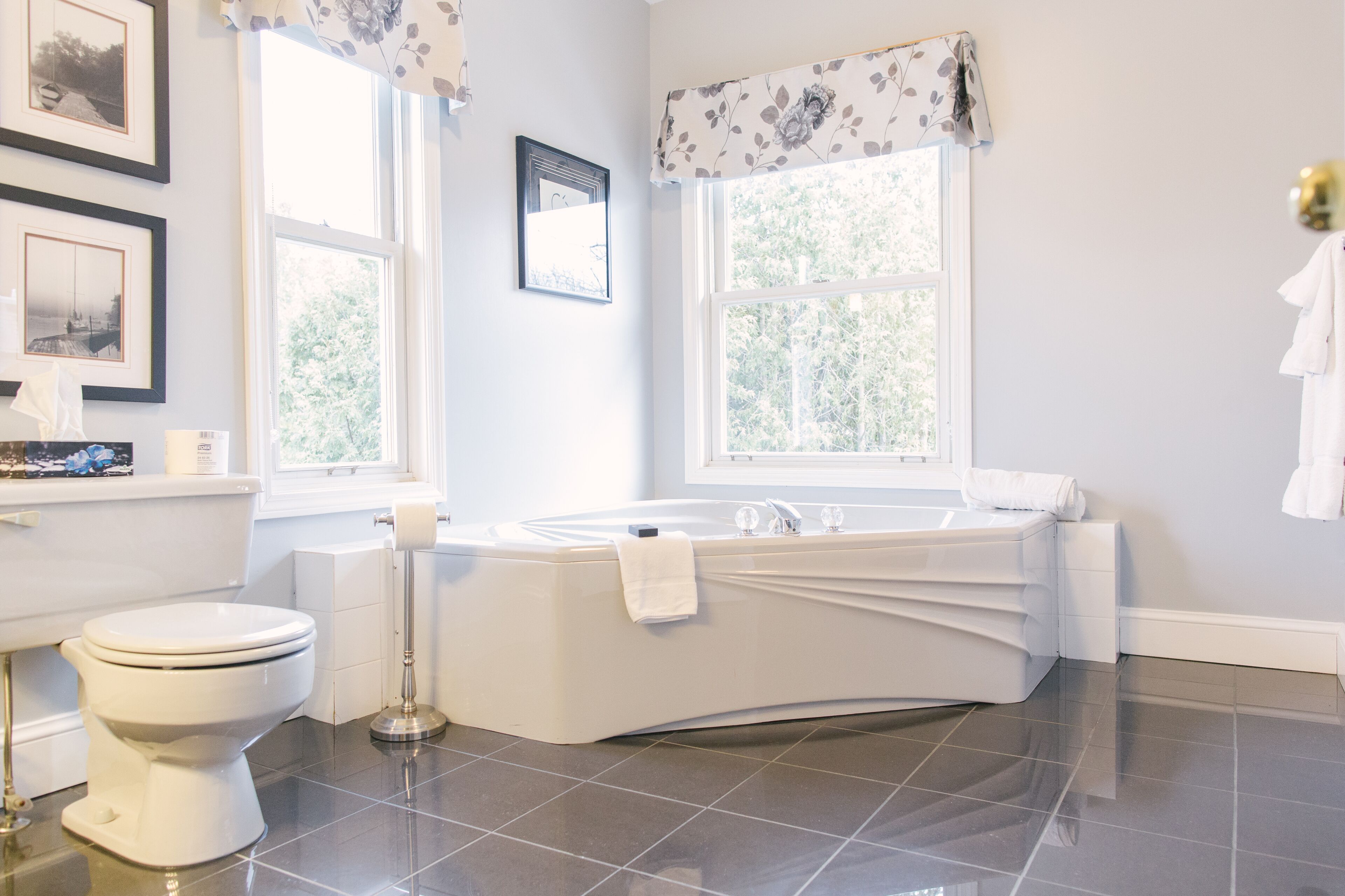 A modern bathroom with a toilet, sink, and bathtub. There are framed pictures on the wall and a window providing natural light.