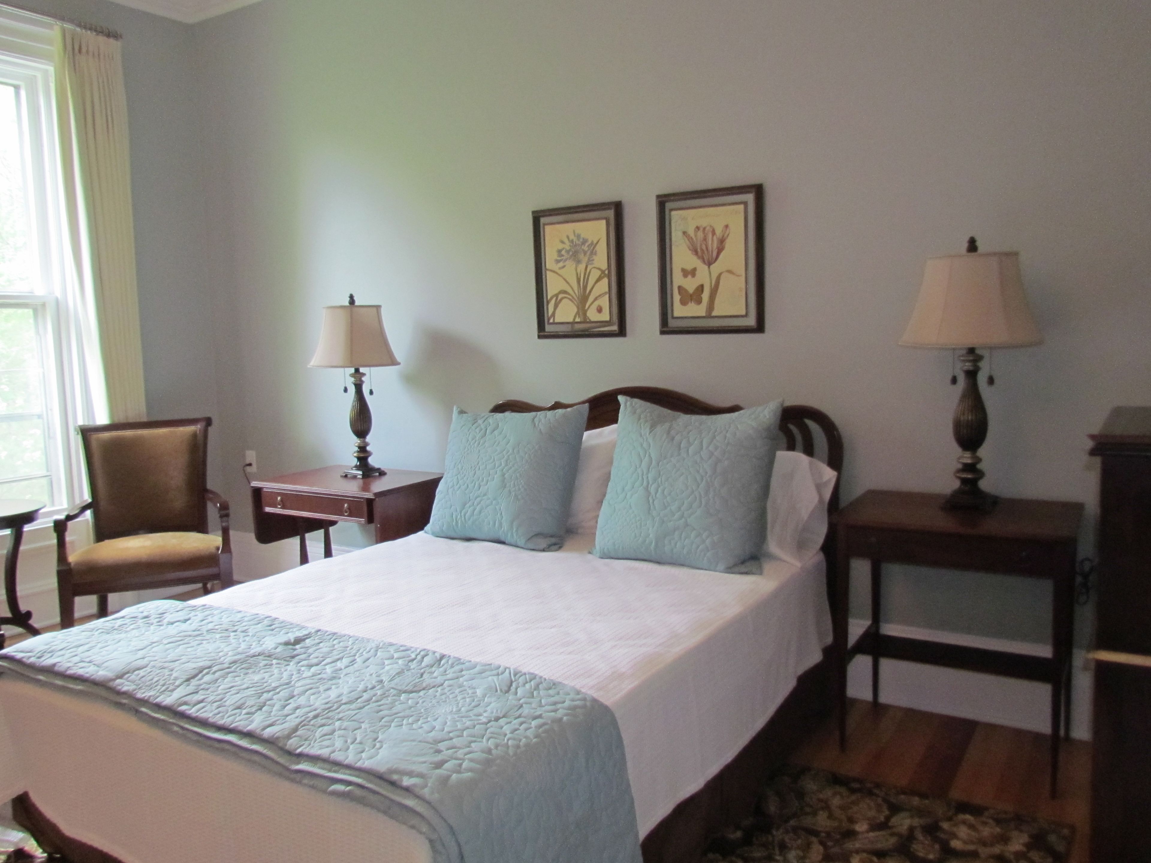 A neatly arranged bedroom with a bed, two bedside tables, a chair, and two wall-mounted lamps.