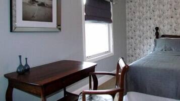 A bedroom with a bed, a wooden desk, a chair, and a framed picture on the wall.
