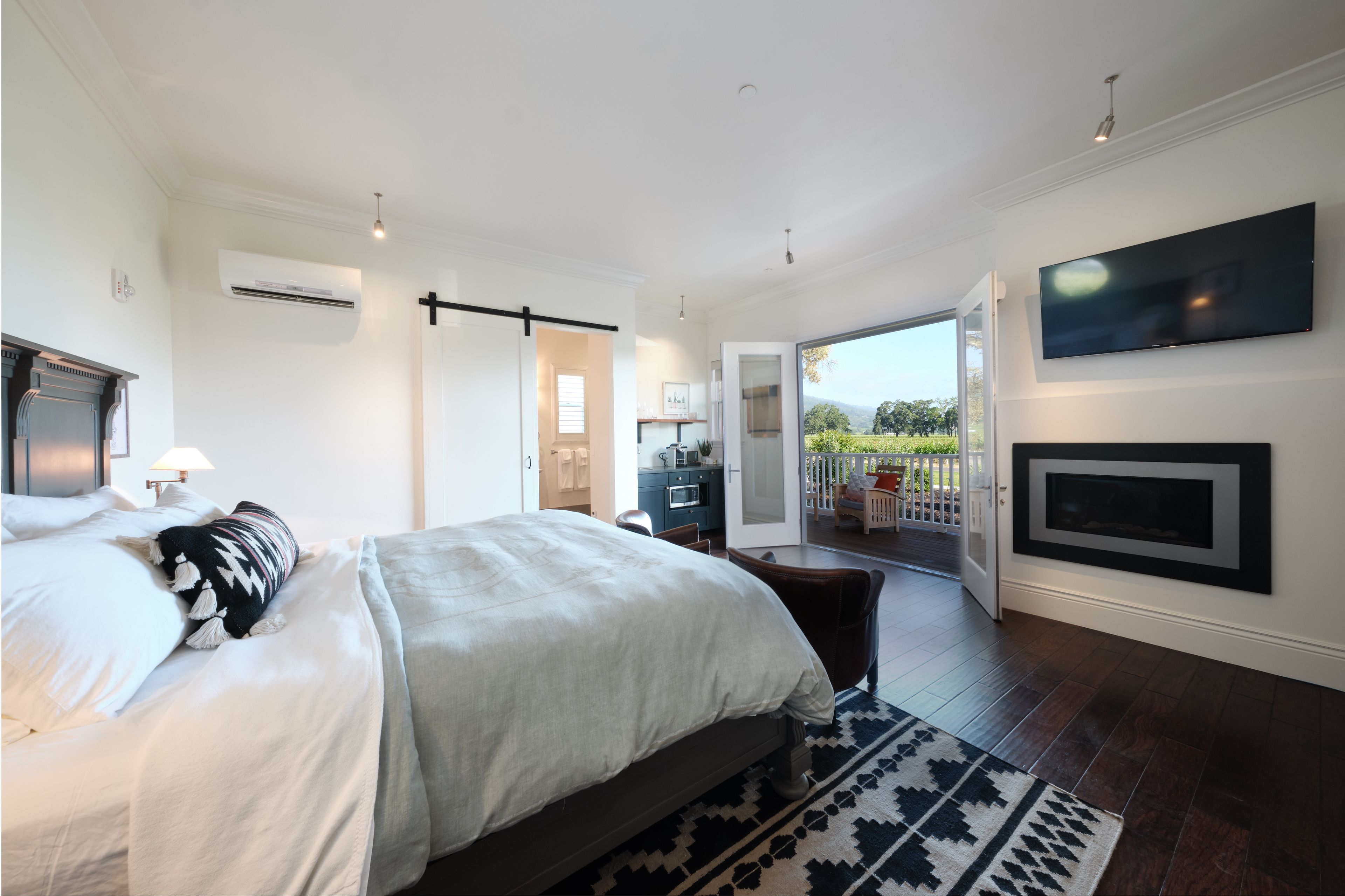 A modern bedroom with a large bed, a fireplace, and a balcony with a view of the outdoors.