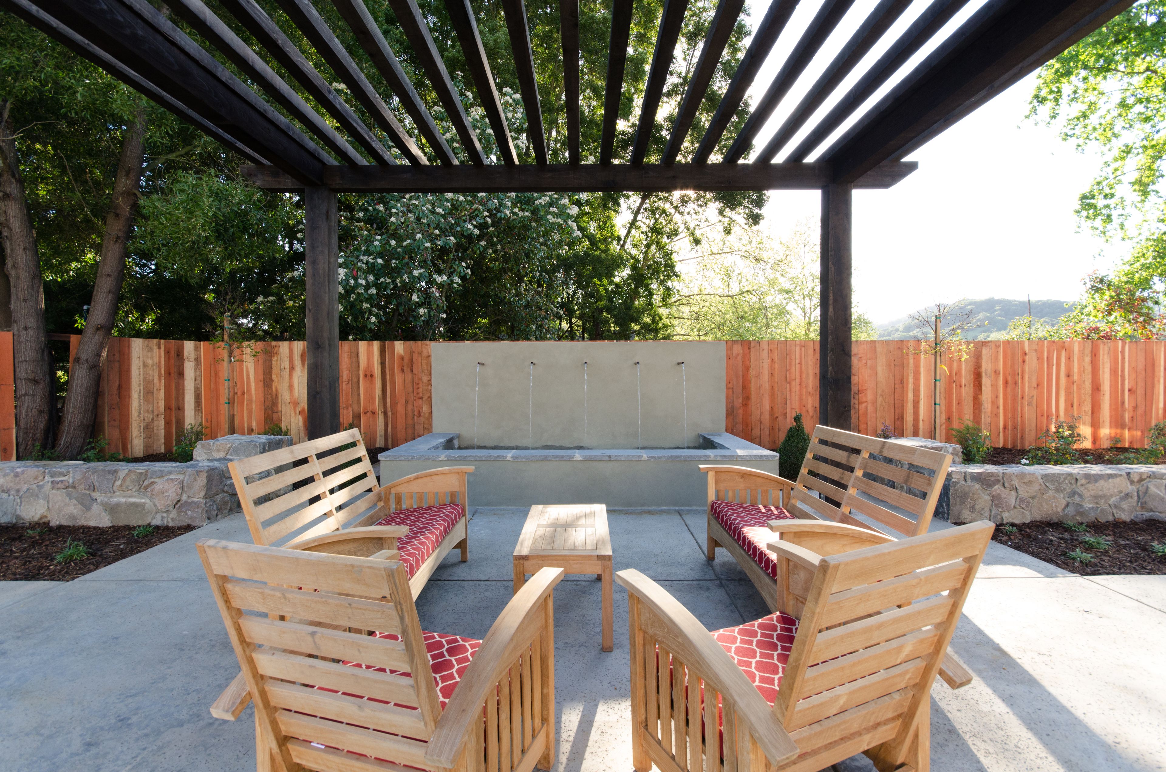 An outdoor patio with wooden furniture, a pergola, and a view of trees and hills.