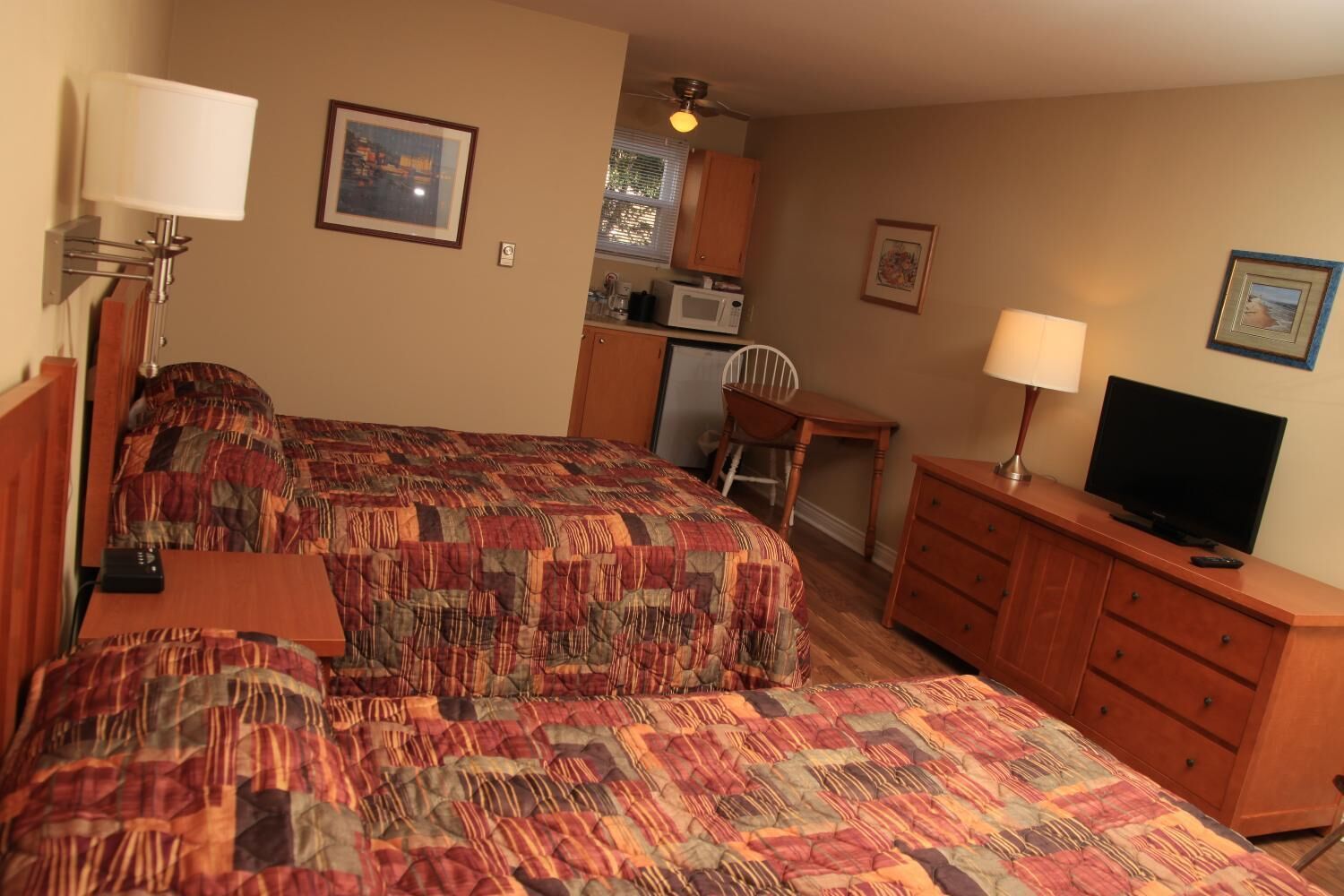 A hotel room with two beds, a TV, a desk, and a kitchenette.