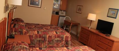 A hotel room with two beds, a TV, a desk, and a kitchenette.