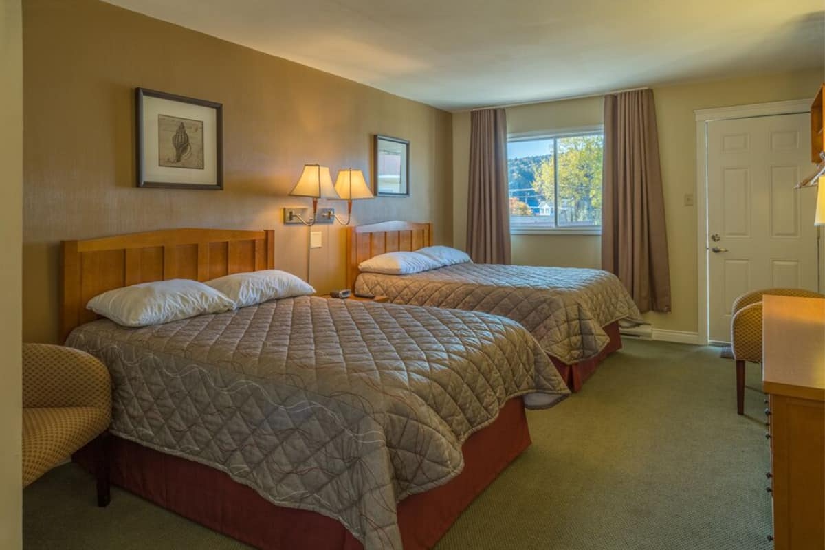 Habitación de hotel con dos camas, una ventana con cortinas, una puerta y una silla.
