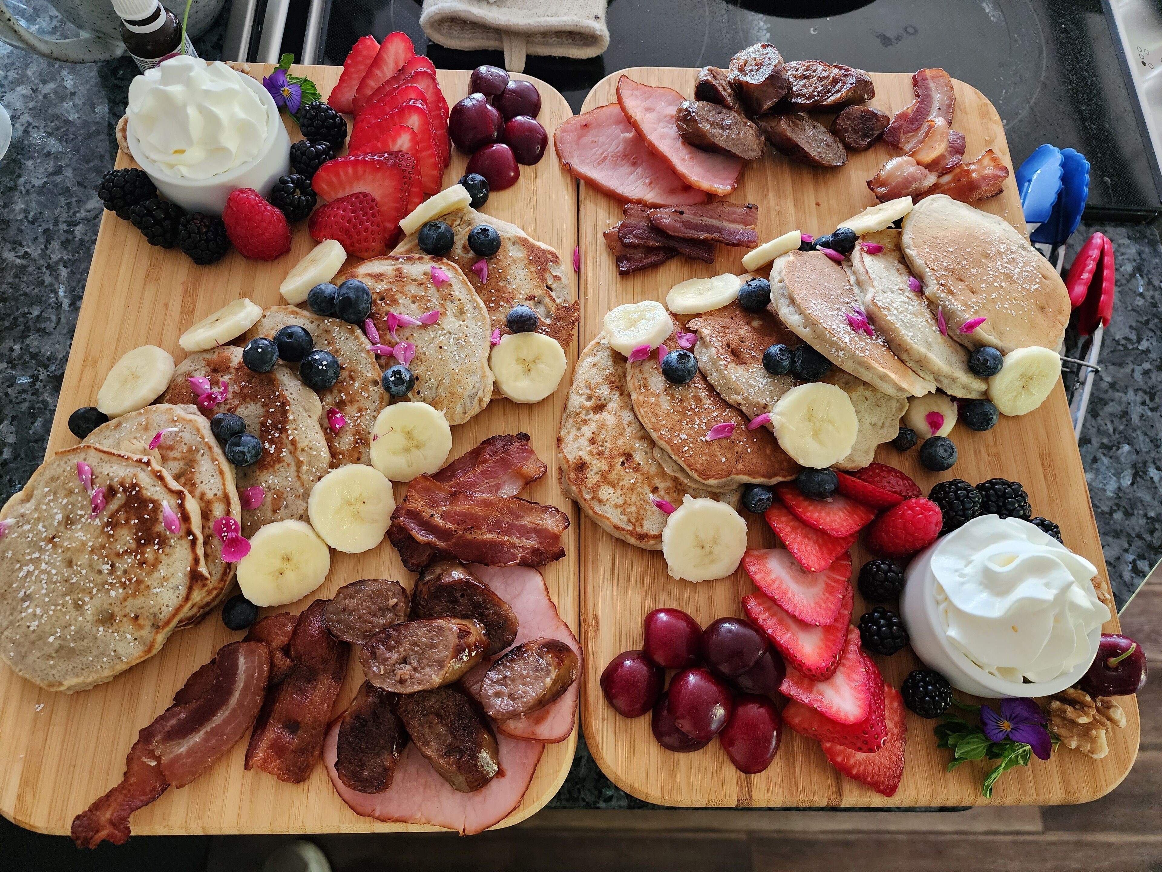 En morgenmadsbakke med pandekager, bacon, skinke, jordbær, blåbær og en skål flødeskum.
