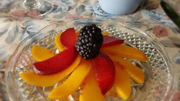 Uma tábua de vidro com frutas fatiadas e um framboeso sobre uma toalha de mesa florida.