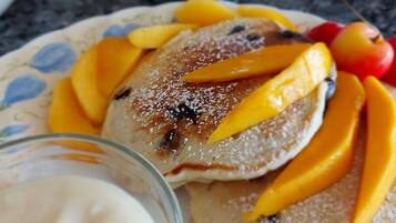 Un plato con panqueques cubiertos de mango en rodajas, una cereza y frambuesas.