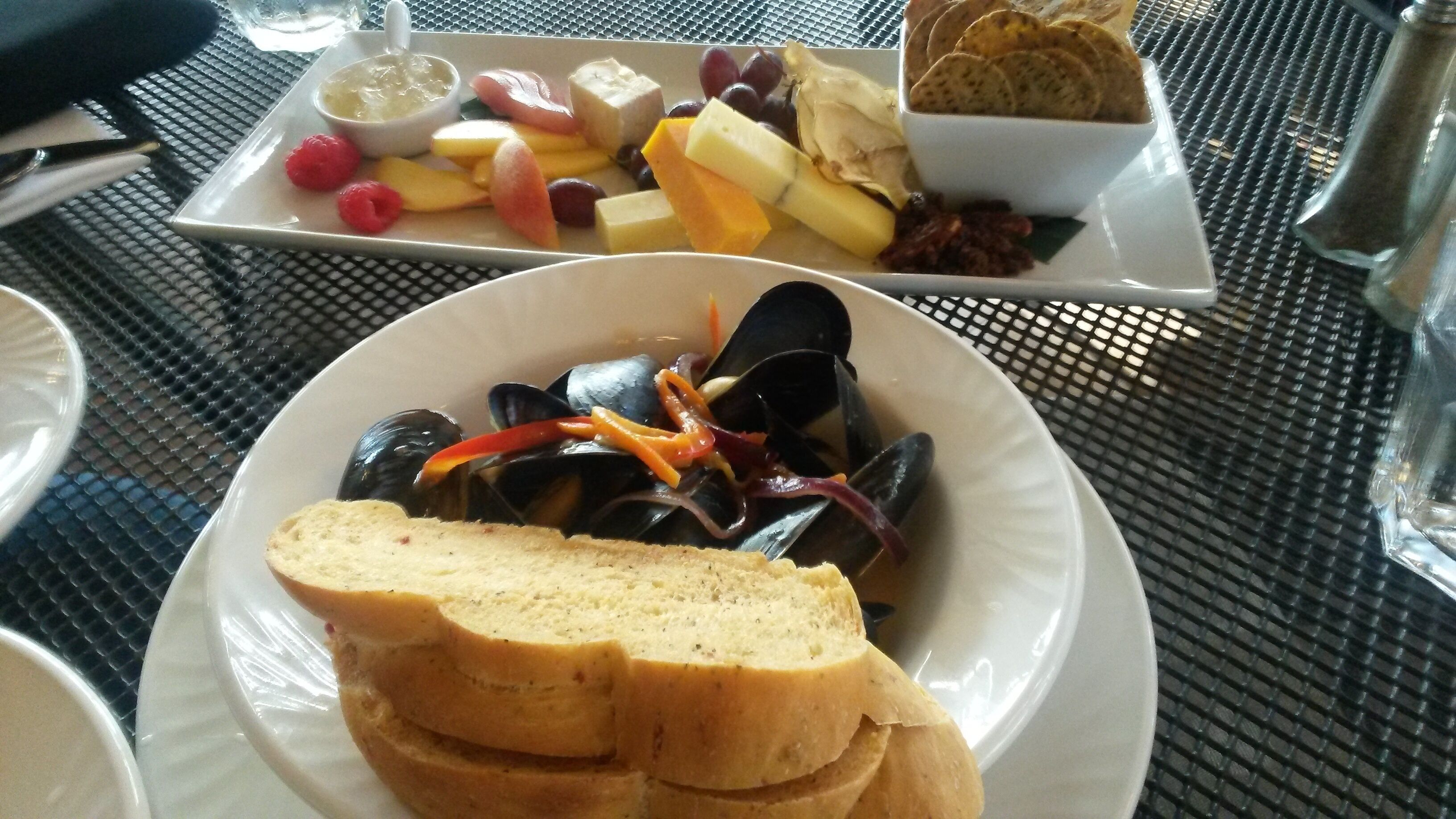 Ein Esstisch mit einer Platte Miesmuscheln, Brot und einer Schüssel mit Obst und Käse.